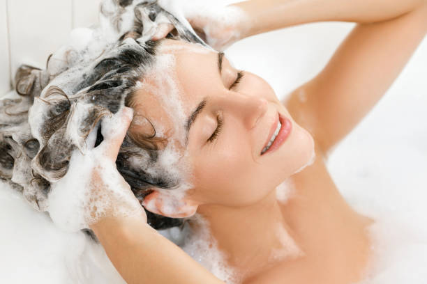 Young and beautiful woman is washing her hair with shampoo